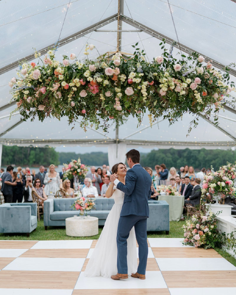 Bride and groom first dance under floral hoop ceiling installation in wedding reception tent