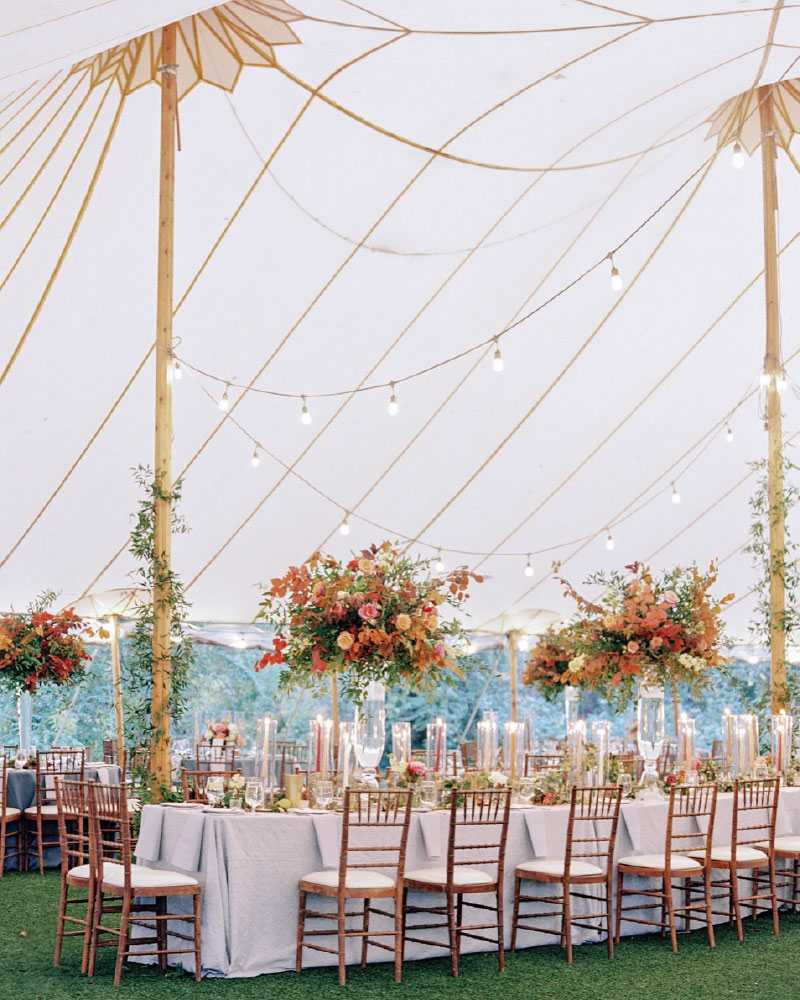 Head table under outdoor wedding tent decorated with taper candles and trumpet vase fall florals